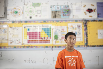 A boy looking at a clear see-through board showing scientific equations and calculations, 