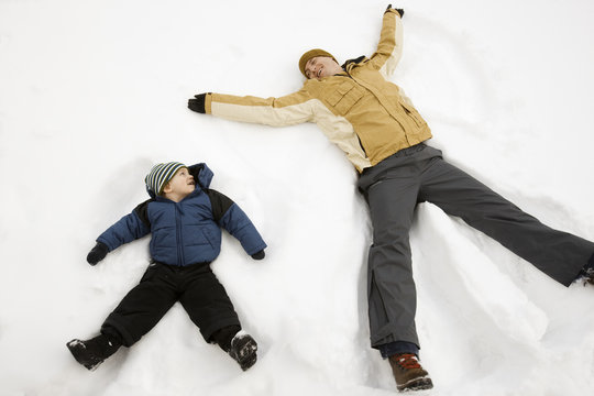 Two people, a man and a child lying in the snow make snow angel shapes, 