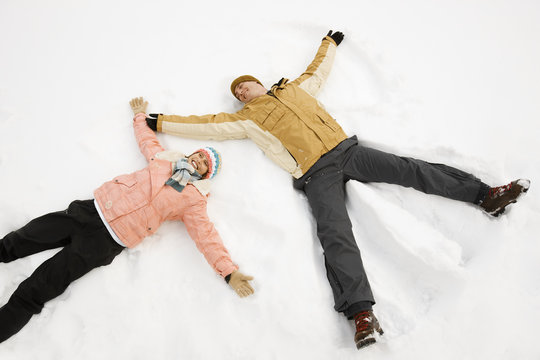 Two people, a man and woman lying in the snow make snow angel shapes, 