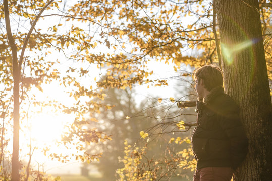 Young Man In Winter Jacket Leaning On A Tree Trunk