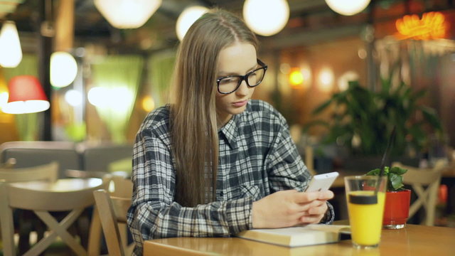 Girl wearing glasses and texting on smartphone in the cafe

