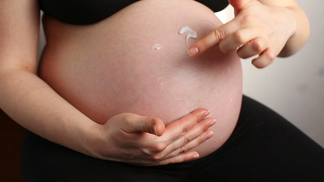 A pregnant woman applying a lotion on her belly