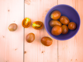 Cherry tomatoes on a blue bowl with cut opened pieces on wooden