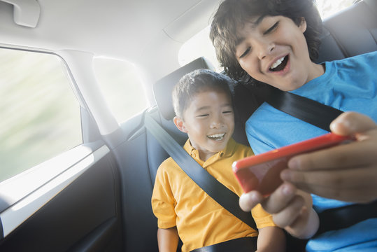 Two children travelling in the back seat of a car sharing a handheld games tablet, 