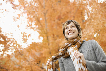 A woman in a jacket and neck scarf against a backdrop of autumn trees in vivid colour,