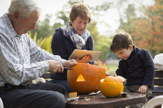 Two adults and a small child with large pumpkins, creating pumpkin lanterns for Halloween, 