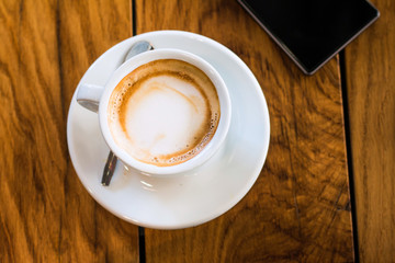 A cup of coffee and smart phone on a woden table in cafe