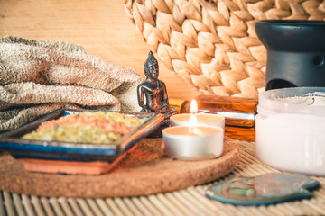 Buddha in meditation, surrounded by candles, stones and oil on a bamboo Mat. Buddha in focus, in the light of a candle.