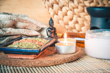Buddha in meditation, surrounded by candles, stones and oil on a bamboo Mat. Focus on the candle.