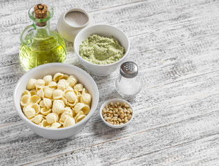 Raw ingredients for making a vegetarian pasta - orecchiette pasta, broccoli and pine nuts pesto sauce, olive oil on a light wooden background