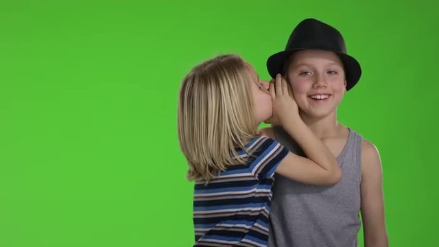 Brother whispers a joke to older brother in front of greenscreen
