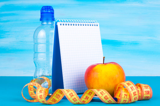 Workout and fitness diet. Healthy lifestyle concept. Apple, bottle of water, measuring tape, notebook.
