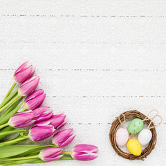 Easter background. Pink tulips, Easter eggs in small nest on white tablecloth. Top view, copy space