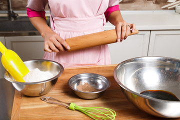Young woman standing with wooden rolling pin near the table
