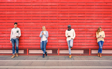 Group of multiracial fashion friends using smartphone with red wood background - Technology addiction in urban lifestyle with disinterest towards each other - Addicted people to modern mobile phones