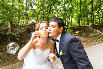 elegant stylish groom and happy gorgeous  bride have fun with bubble blower outdoors in park