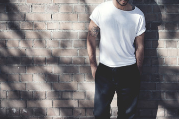 Photo bearded man with tattoo wearing blank white tshirt and black jeans. Bricks wall background....