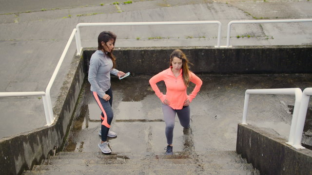 Fitness female trainer encourage a woman to complete lunges workout on urban stairs. Women training legs together.