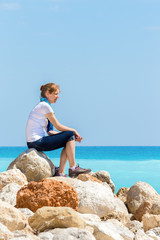 Fototapeta na wymiar Caucasian woman sitting on rocks at coast near sea