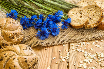 Whole wheat bread rolls with ears of cereal on wood