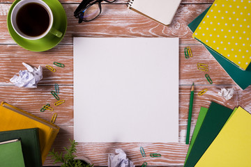 Office table desk with supplies, white blank note pad, cup, pen, pc, crumpled paper, flower on wooden background. Top view