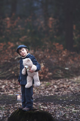 Cute little child, holding lantern and teddy bear in forest