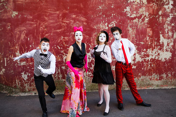 Four mimes standing on a red wall.