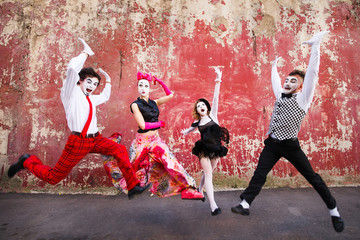 Four mimes jumping on a background of a red wall.