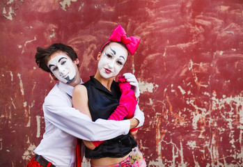 Couple mimes cute pose in front of a red wall.