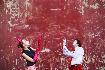 Couple mimes point to the top on a red wall.
