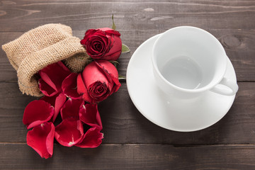 Red roses flowers and a cup are on the wooden background