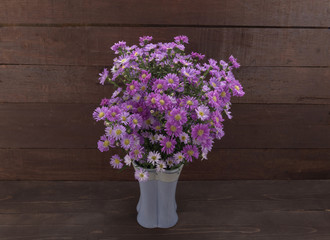 Fototapeta na wymiar Purple cutter flowers in the vase, on the wooden background