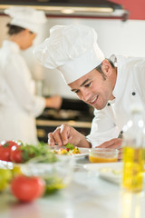 Portrait of a man chef putting herbs on a  plateful