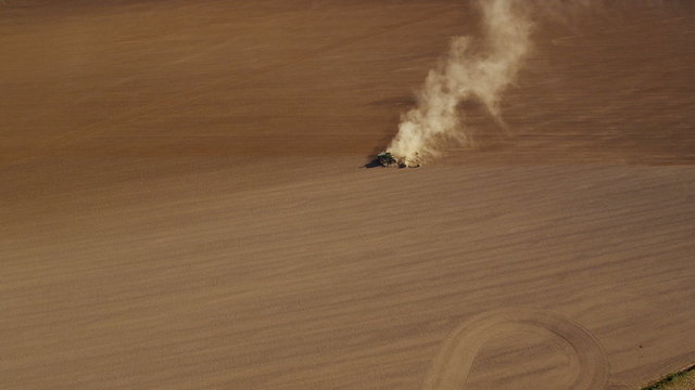 Aerial shot of dust trail behind tractor plowing