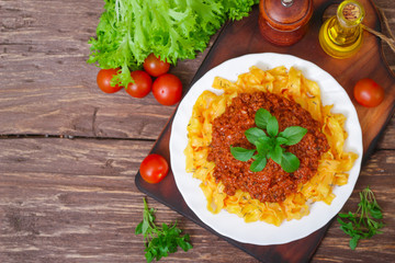 Traditional Italian pasta Bolognese or Bolognese with cooked pasta noodles topped with a spicy tomato based meat sauce garnished with fresh basil on a wooden background