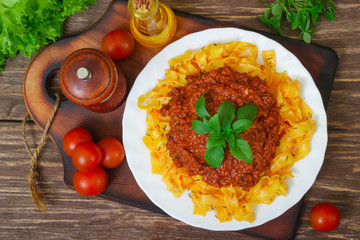 Traditional Italian pasta Bolognese or Bolognese with cooked pasta noodles topped with a spicy tomato based meat sauce garnished with fresh basil on a wooden background