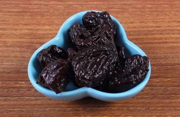 Dried plums in blue bowl on wooden table, healthy food