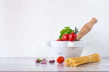 mortaio con pomodori e basilico, accanto pasta e spicchi d'aglio; spazio vuoto