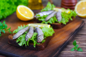 Traditional Spanish sandwiches with anchovies, lettuce and lemon on a wooden background