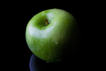 Green fresh ripe apple on black background with reflection from high angle