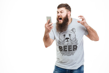 Irritated angry man with beard holding smartphone and shouting