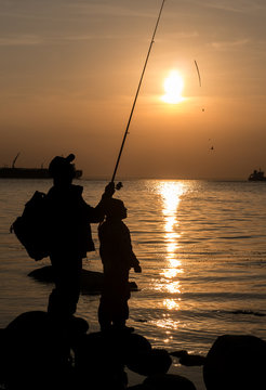 Silhouette of father and daughter fishing with rod at sunset