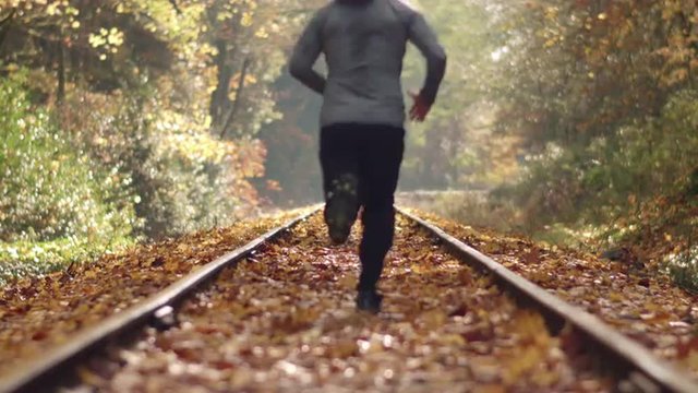 Man Jogging Down Train Tracks in Autumn Season with Leaves Falling Deep Focus