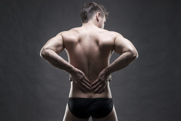 Fototapeta na wymiar Kidney pain. Man with backache. Handsome muscular bodybuilder posing on gray background. Low key close up studio shot