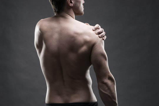 Pain in the shoulder. Muscular male body. Handsome bodybuilder posing on gray background. Low key close up studio shot