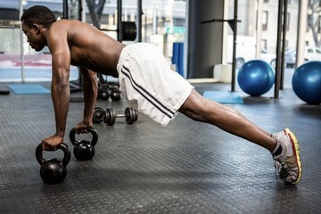 Muscular man doing push up with kettlebells