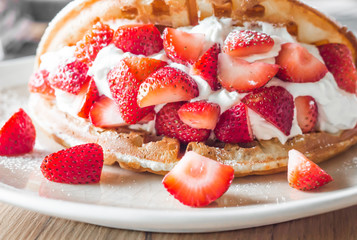 Strawberries waffles with vanilla ice cream on white plate.