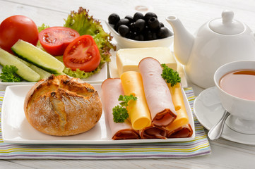 Healthy breakfast with cheese, ham, fresh bun, fresh vegetables, olives and tea. 