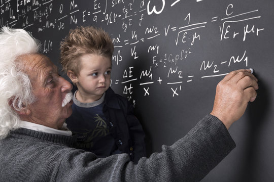 Nonno scienziato che scrive alla lavagna con nipotino in braccio