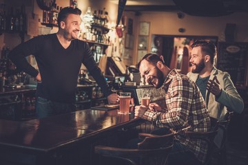 Fototapeta na wymiar Cheerful old friends having fun and drinking draft beer at bar counter in pub.